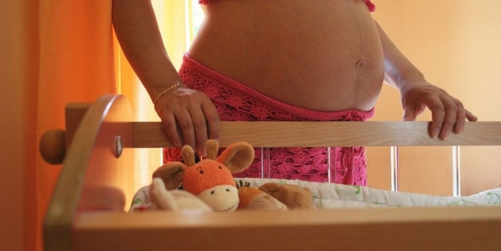 pregnant woman beside a crib